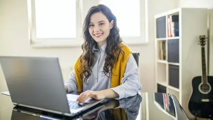 Junge Frau sitzt lächelnd an einem Tisch mit ihrem Laptop Junge Frau arbeitet am Laptop